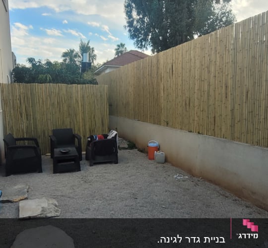 חצר עם גדר במבוק, כיסאות פלסטיק ואבנים על הקרקע